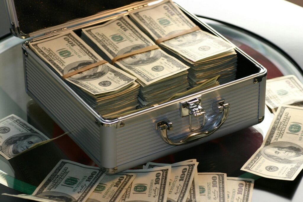 Open briefcase filled with stacks of hundred dollar bills on a glass table, representing wealth and growth