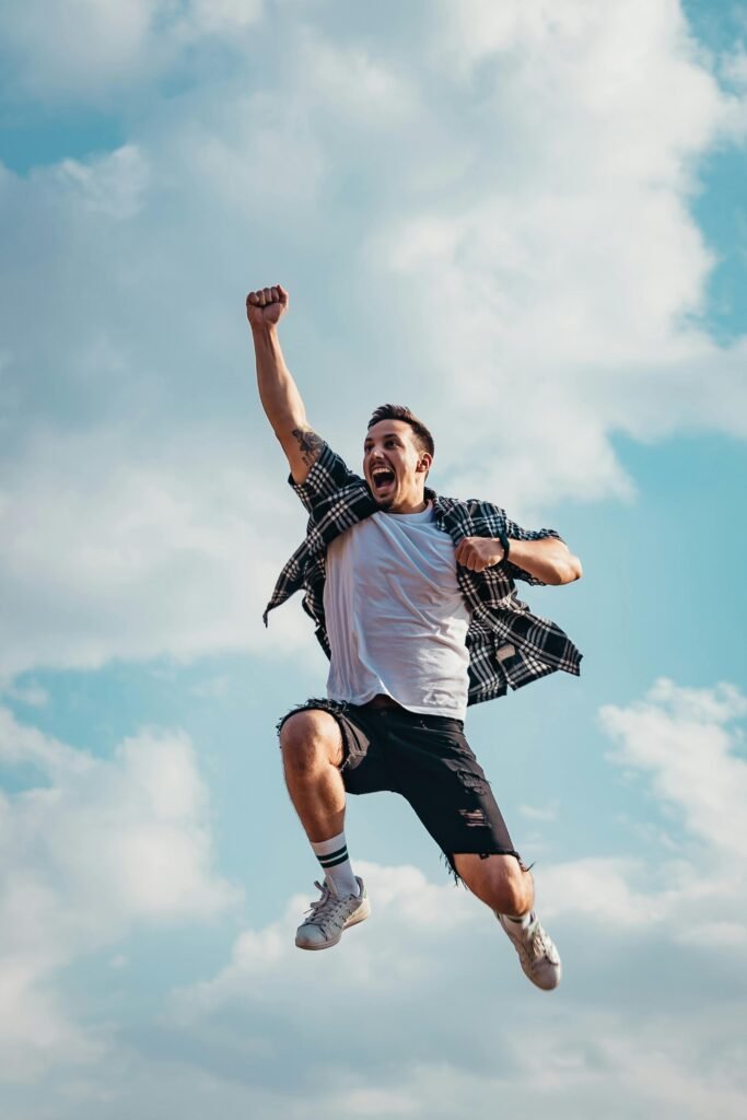 A joyful young man jumps midair with clouds and blue sky in the background, exuding energy and freedom.invest-in