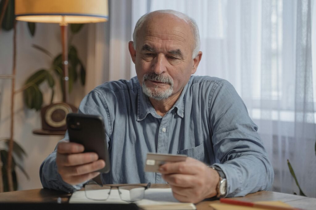 An elderly man using a smartphone and credit card for online shopping at home - showcasing the convenience mobile apps usage offers