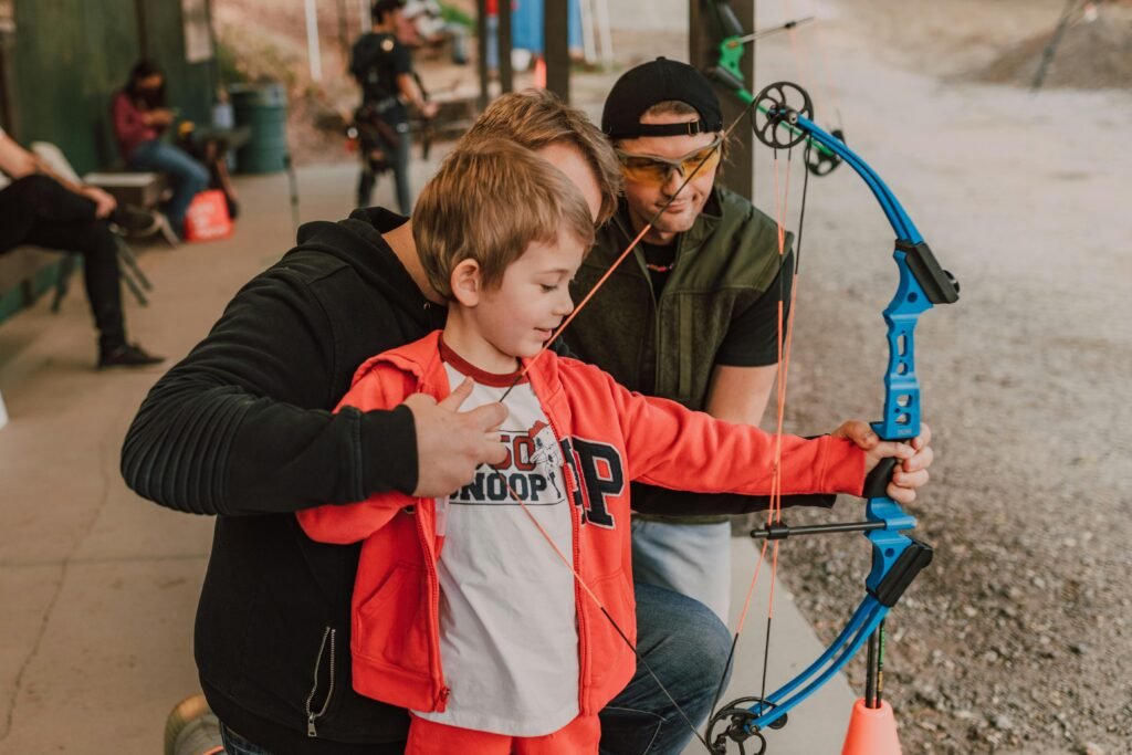 Child learning archery with guidance and support, embracing outdoor fun.