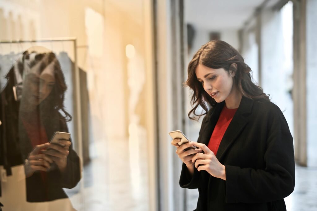Young woman using smartphone at a store window reflecting her image depicting the growing mobile apps usage