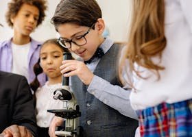 Children in a classroom exploring science with a microscope, emphasizing learning and diversity.